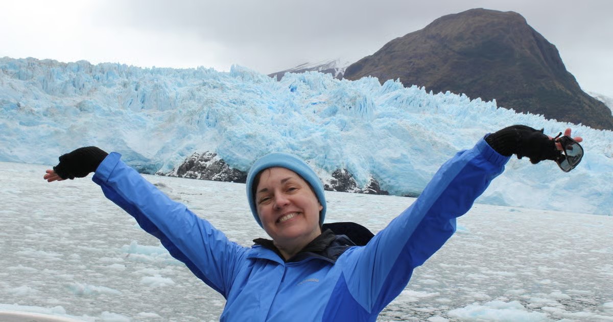 Nicky Penttila with arms raised in front of a glacier in Patagonia